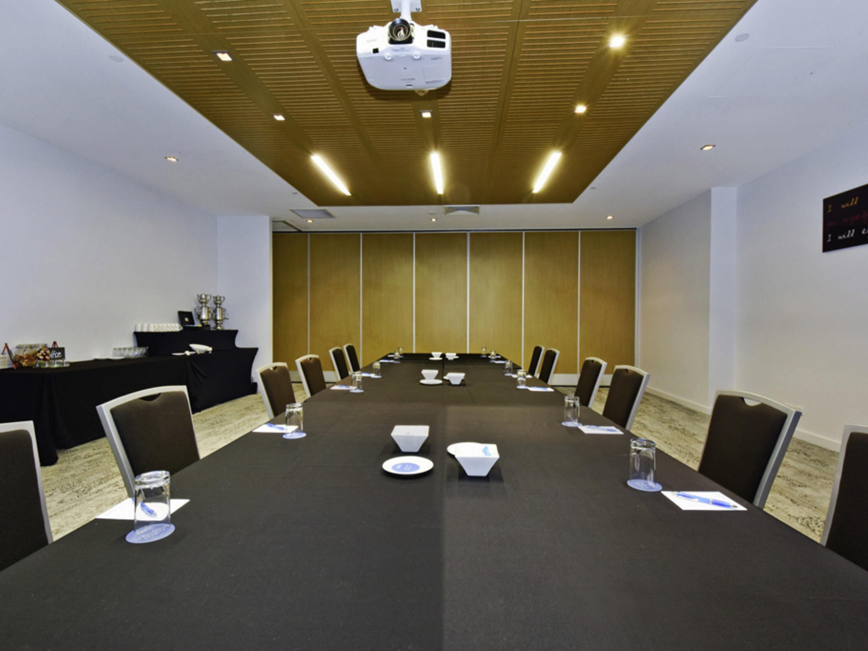 A conference room with a long table, chairs, a projector, and a podium.