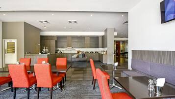 Un moderno vestíbulo de hotel con zona de comedor que incluye sillas rojas y un sofá gris.
