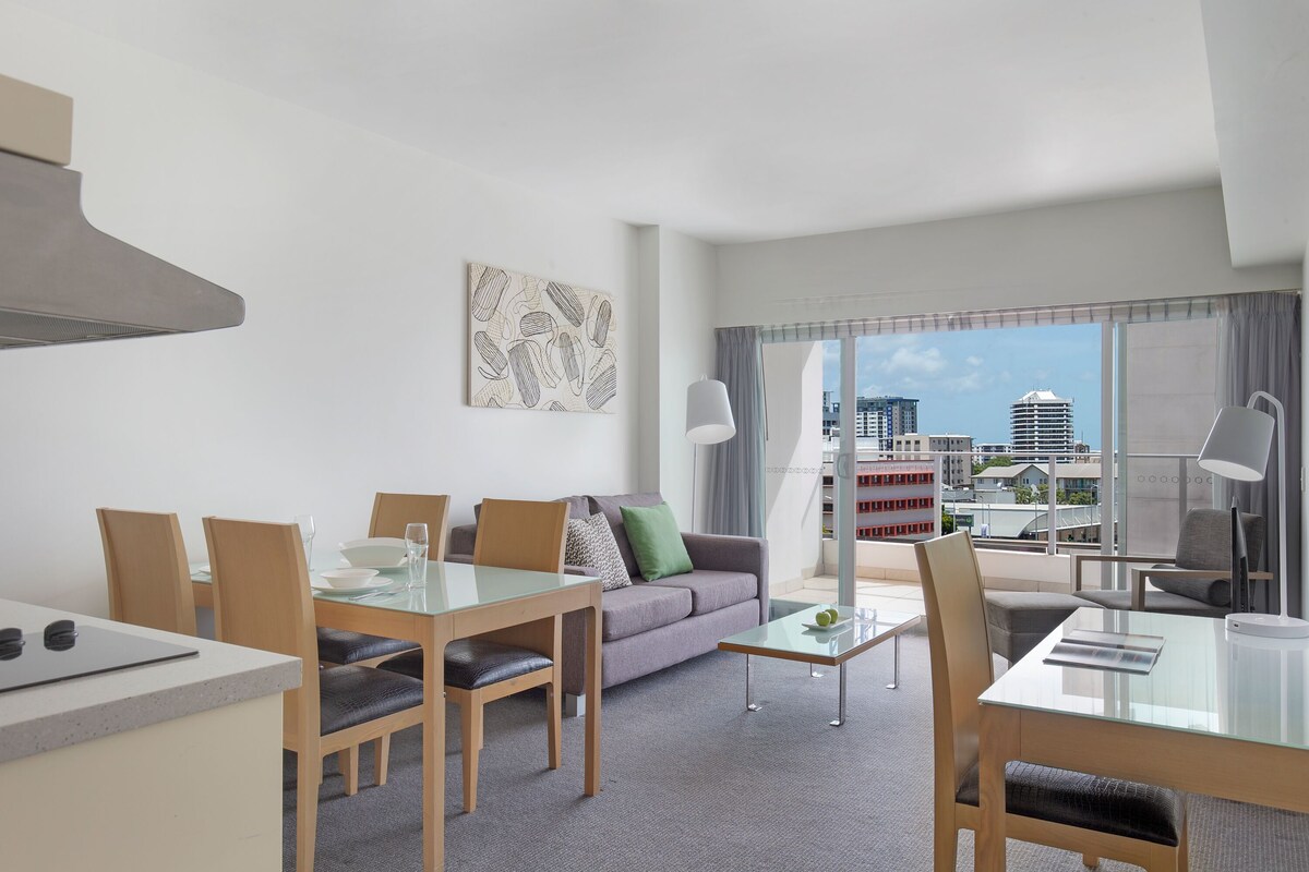 A modern hotel room with a dining area, a sofa, and a balcony with a city view.