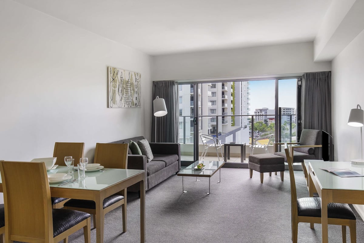 A modern hotel room with a balcony, a sofa, a dining table, and chairs.