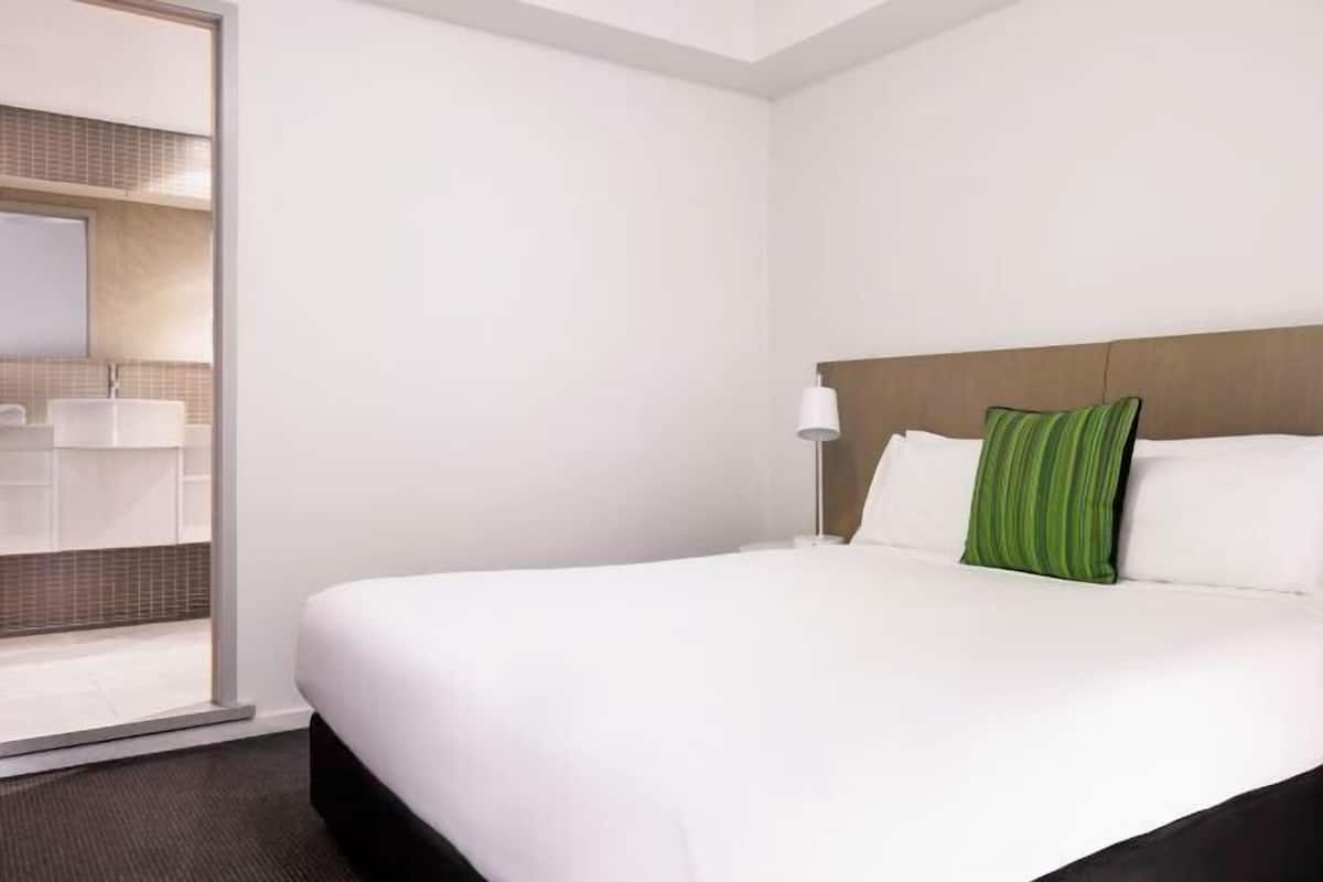 A hotel room with a bed, a nightstand, a lamp, and a view of the bathroom.
