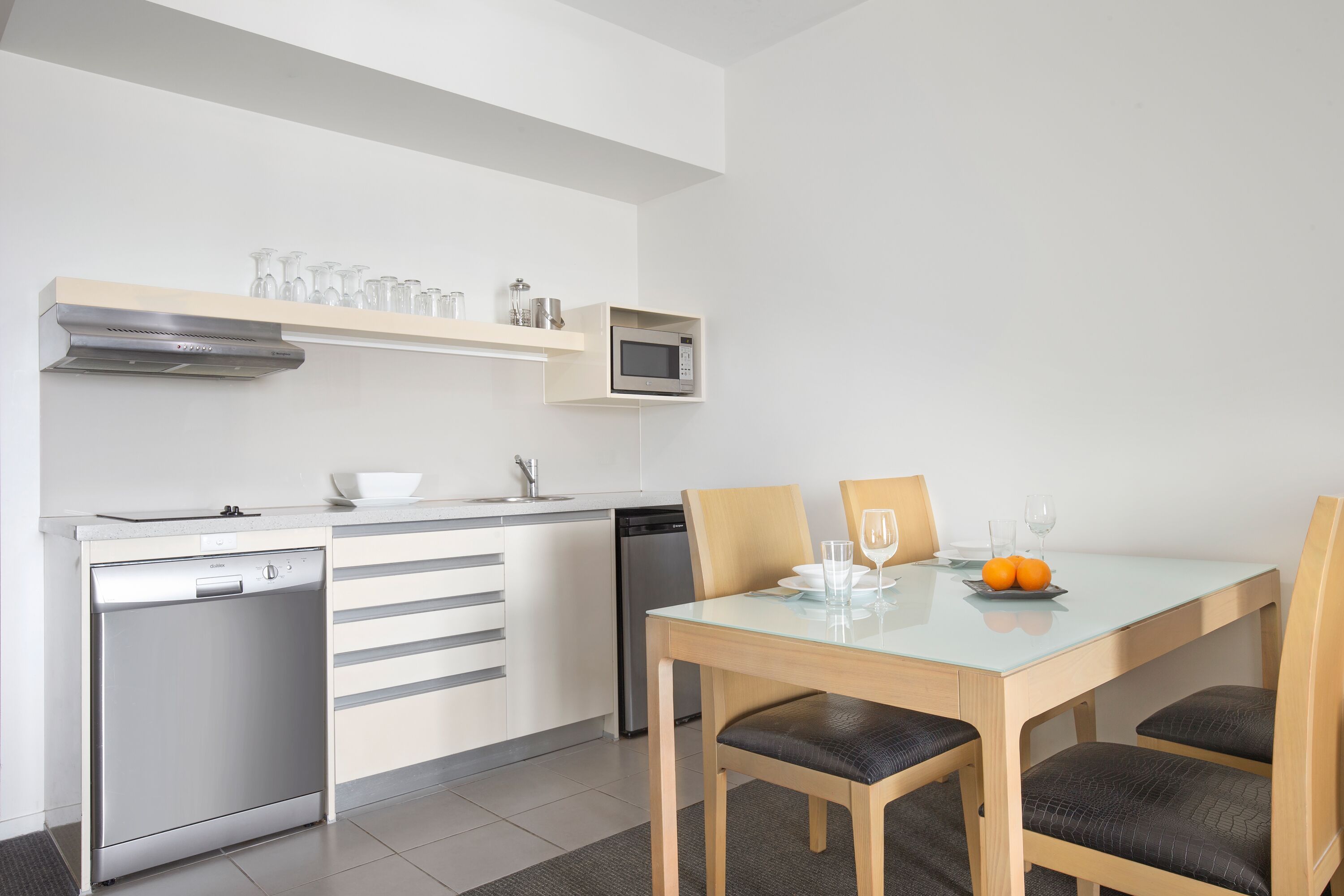 A modern kitchen with a dishwasher, microwave, and glass-top dining table with chairs.