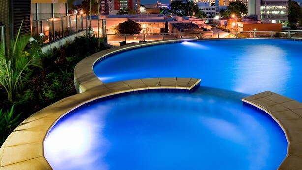A swimming pool with a curved edge, surrounded by a tiled deck and a small bridge. - Mantra Pandanas (Darwin)