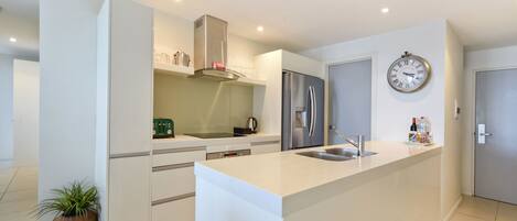 A modern kitchen with white cabinetry, stainless steel appliances, and a built-in island with a sink.