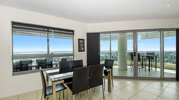 A dining area with a table and chairs, large windows with blinds, and a view of the cityscape.