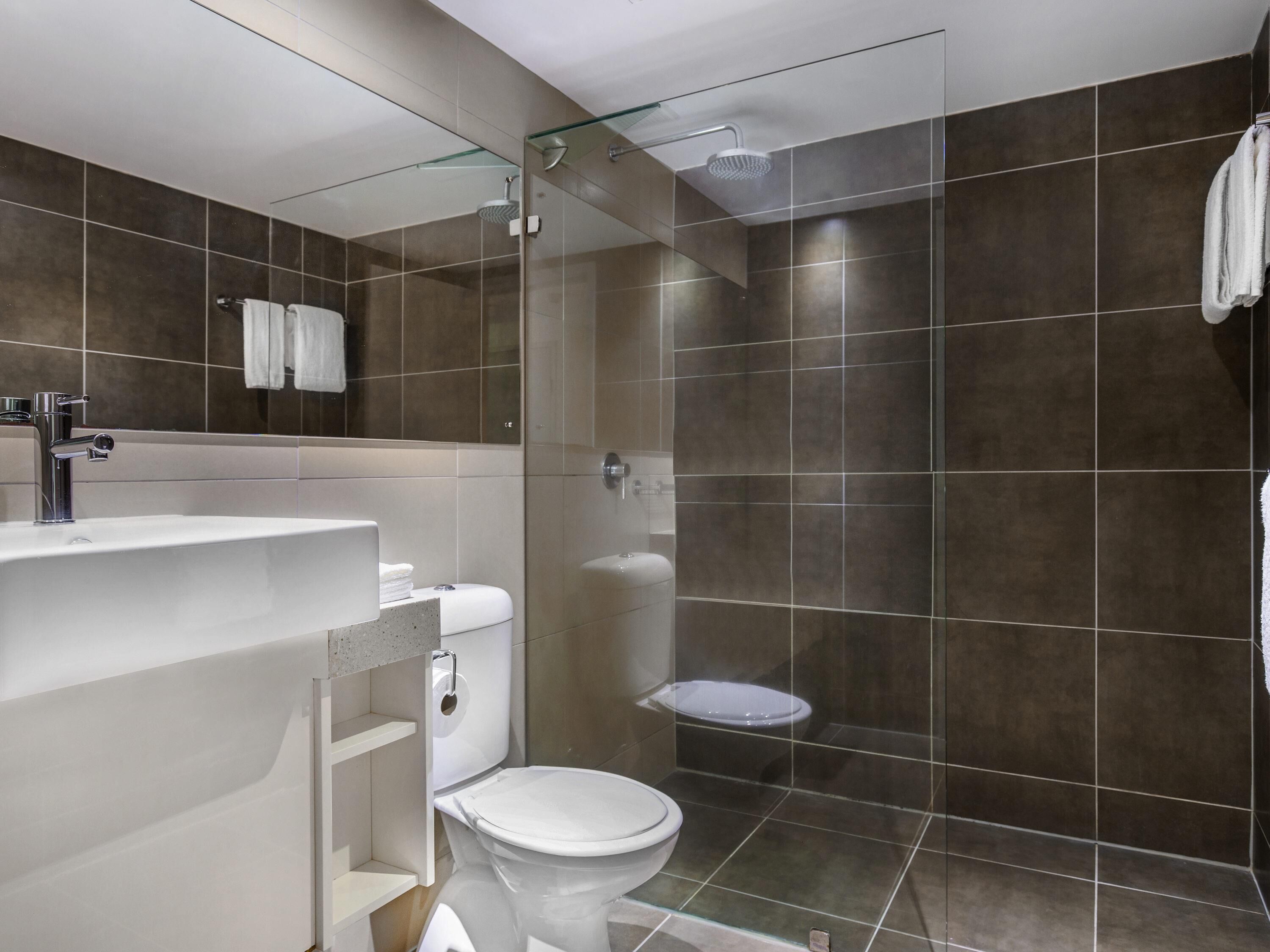 A modern bathroom with a glass shower enclosure, a white toilet, and a sink with a mirror.