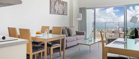 Una habitación de hotel moderna con zona de comedor, sofá y balcón amplio con vista a la ciudad.