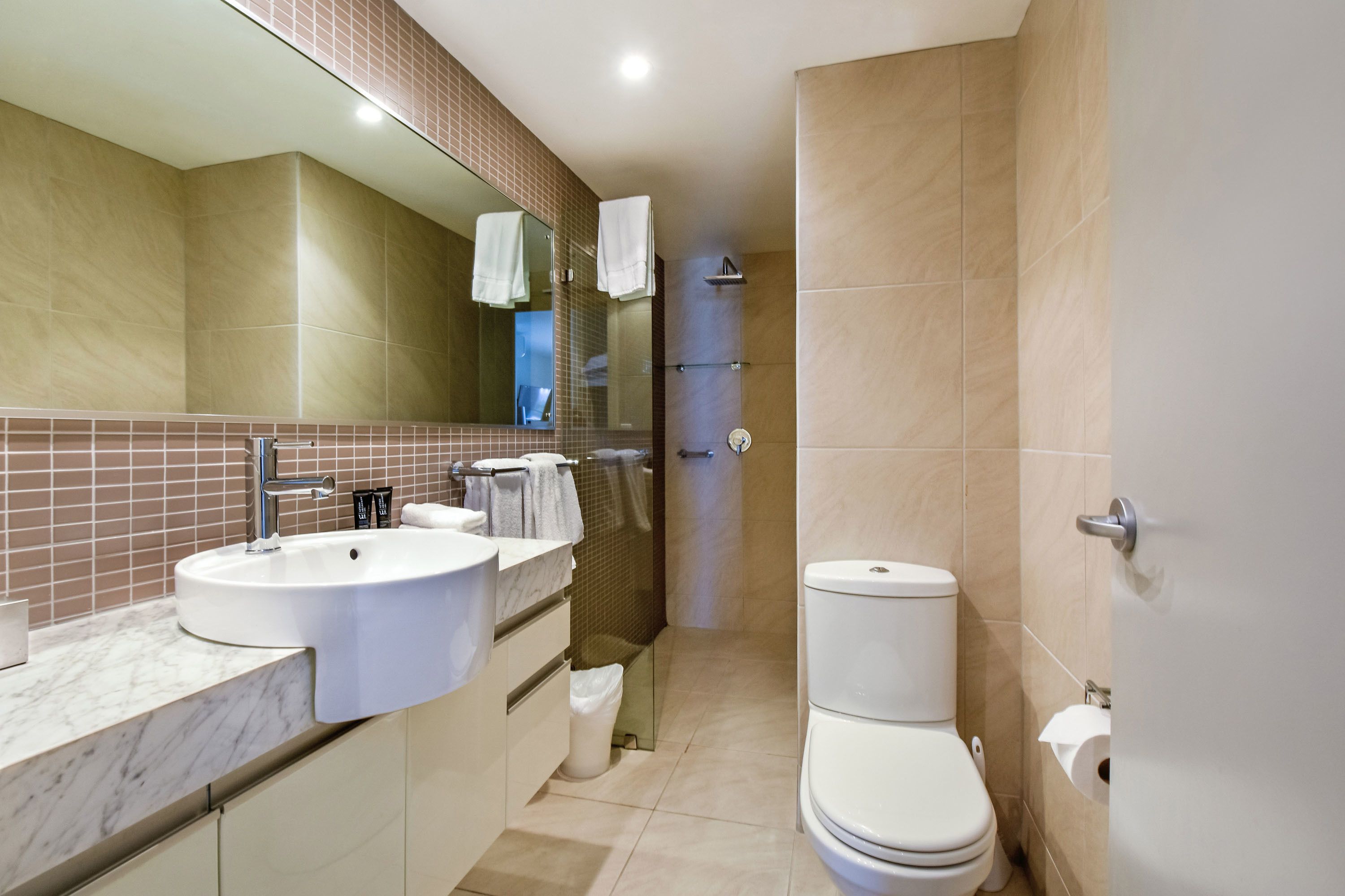 A modern bathroom with a large mirror, two sinks, a toilet, and a shower area.
