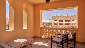 A room with a bed, a table with a chair, and a view of an outdoor area with umbrellas.