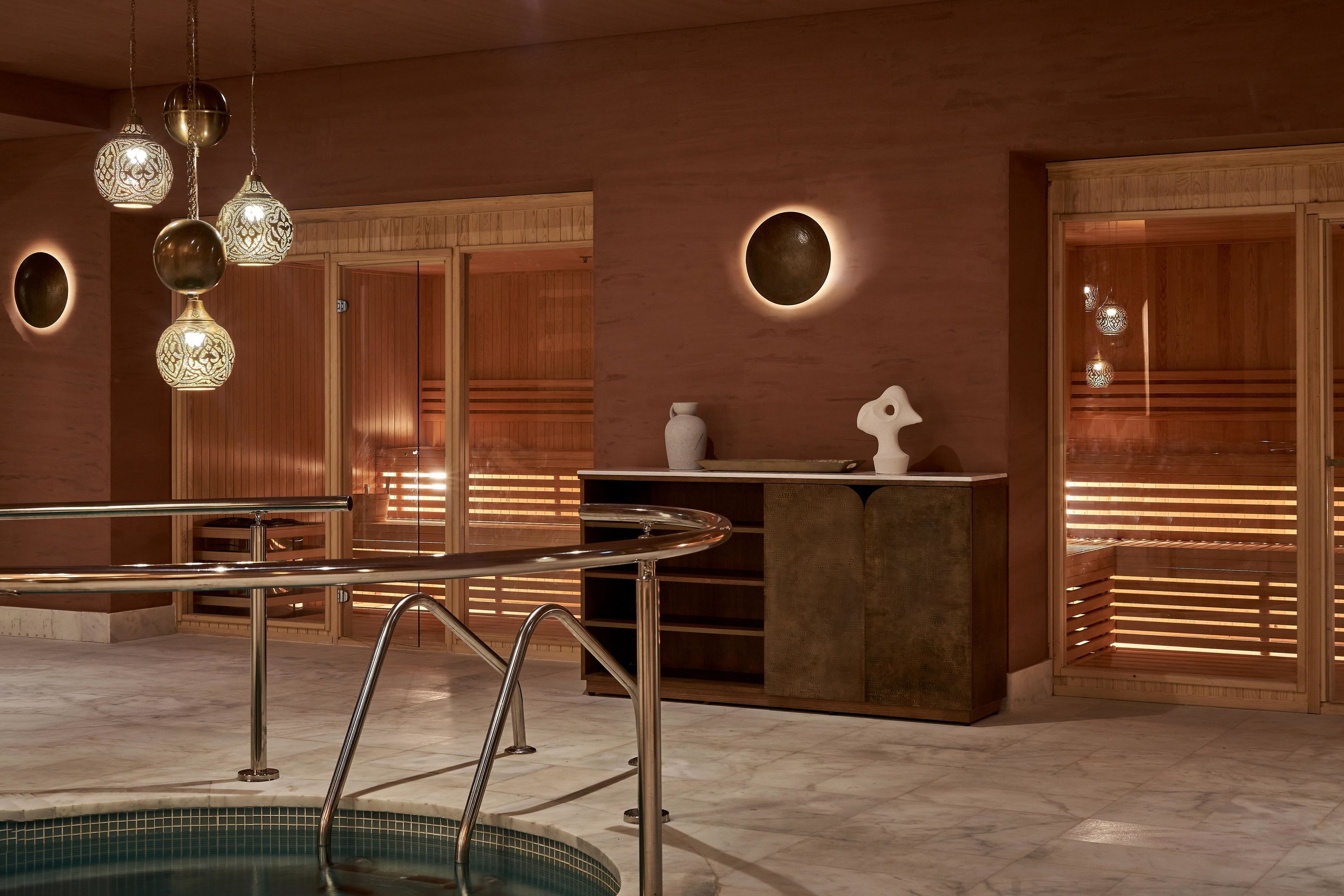 Un moderno espacio de spa con piscina, barandillas metálicas e iluminación decorativa.