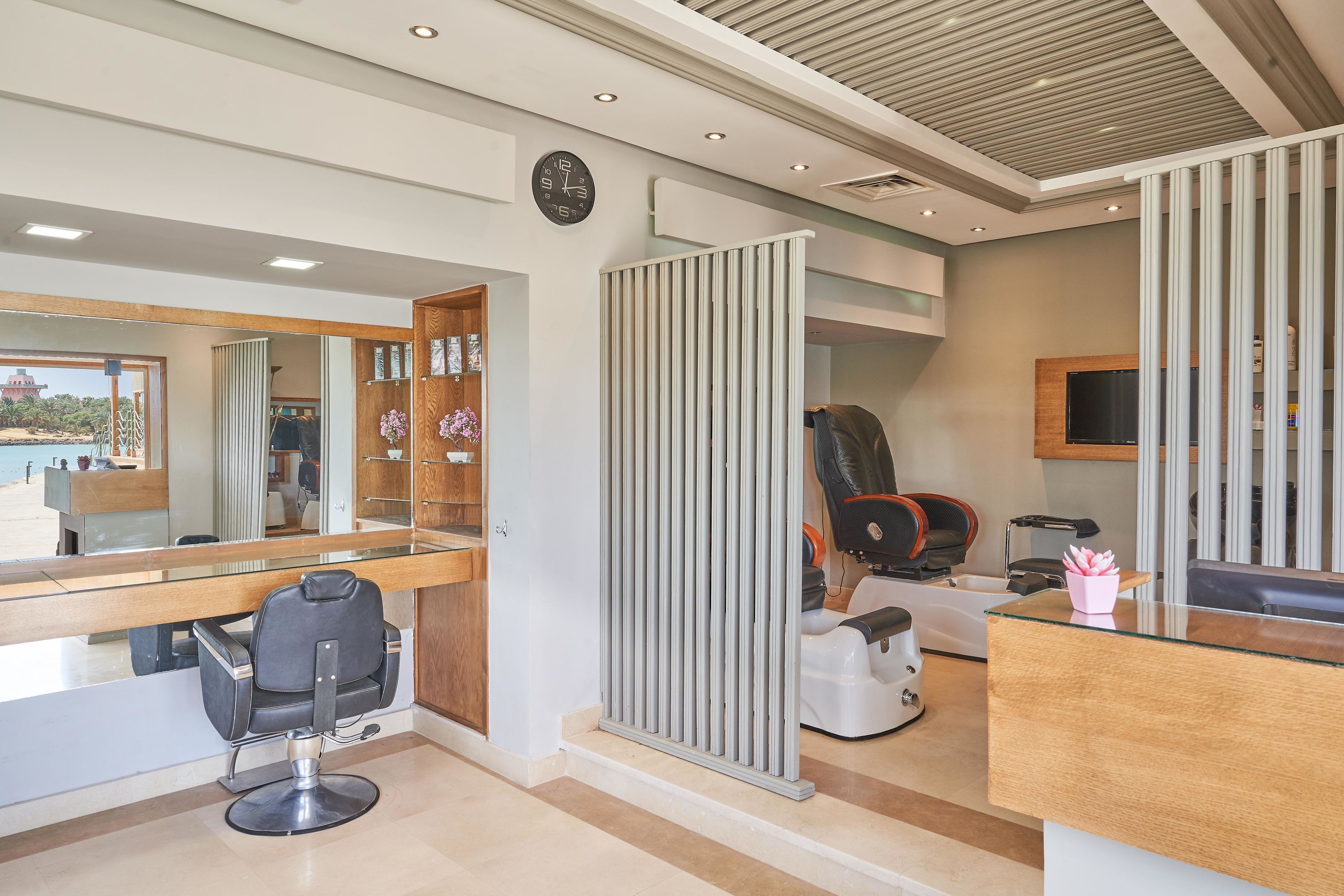 Un moderno salón de belleza con un espejo grande, una estación de lavado de cabello y una pantalla de televisión.