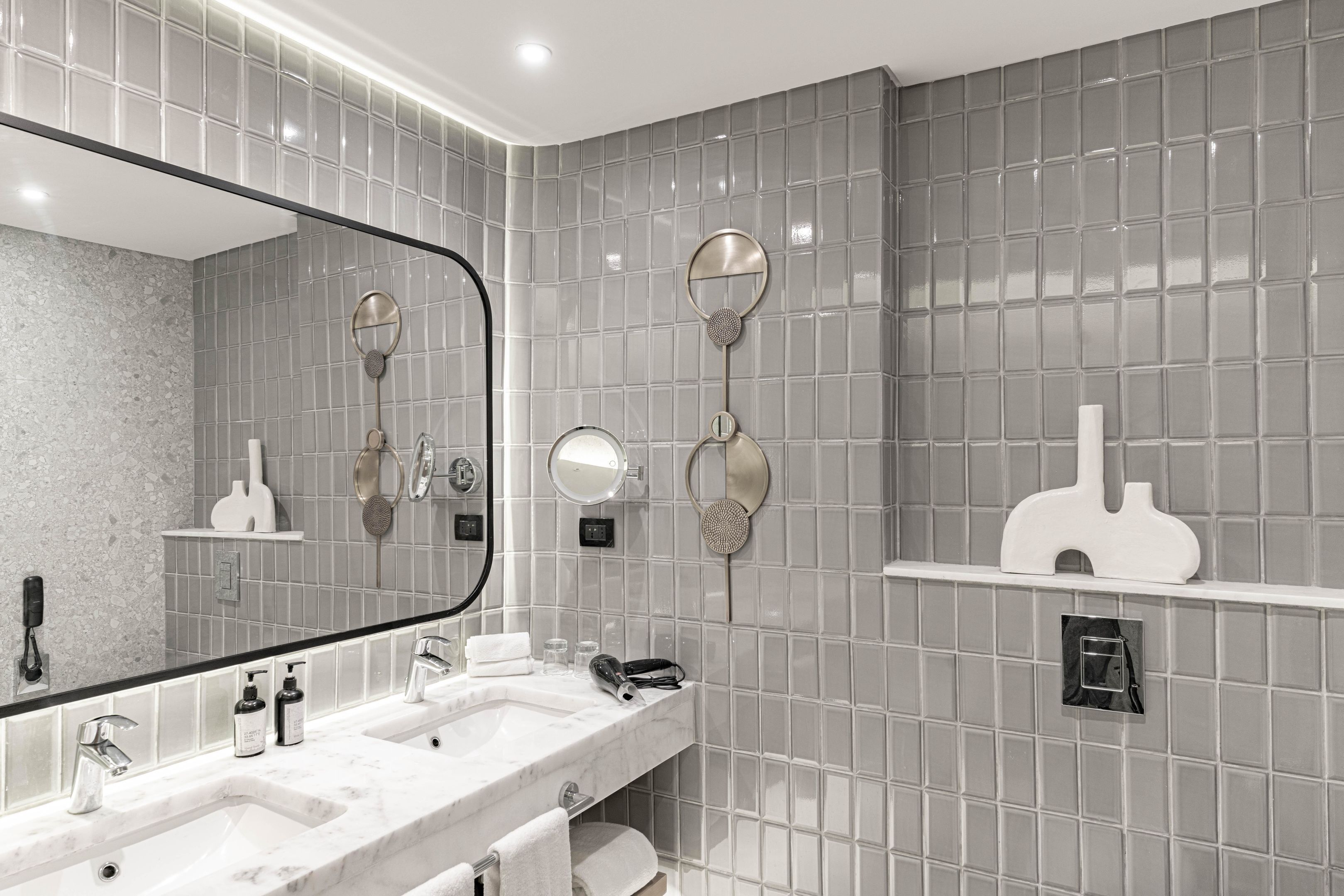 Ein modernes Badezimmer mit zwei Waschbecken, einem großen Spiegel und gefliesten Wänden.