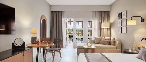 A hotel room with a bed, a desk with a lamp, a chair, a sofa, and a view of the outside.