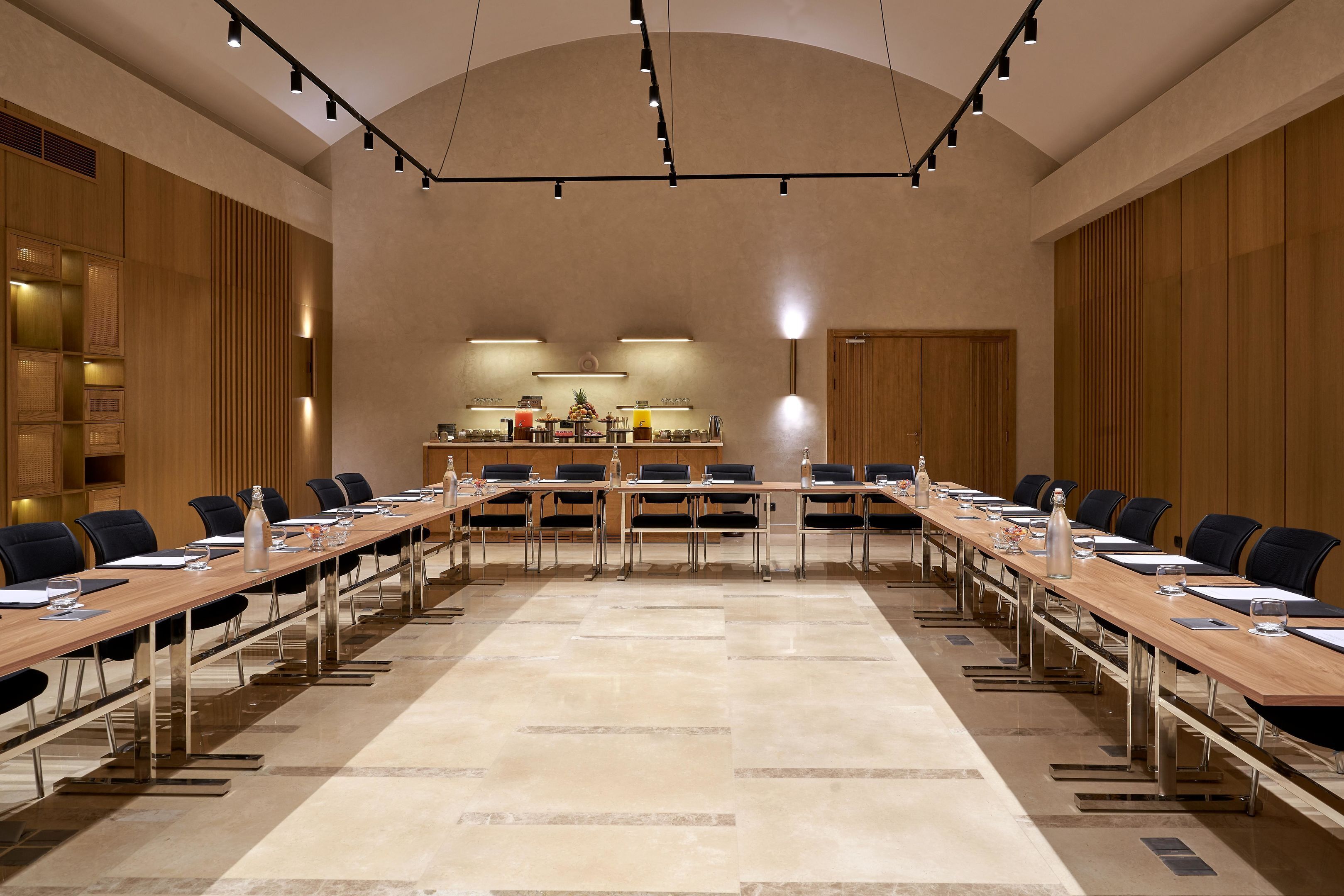 A conference room with a long table, chairs, and a kitchen area in the background.