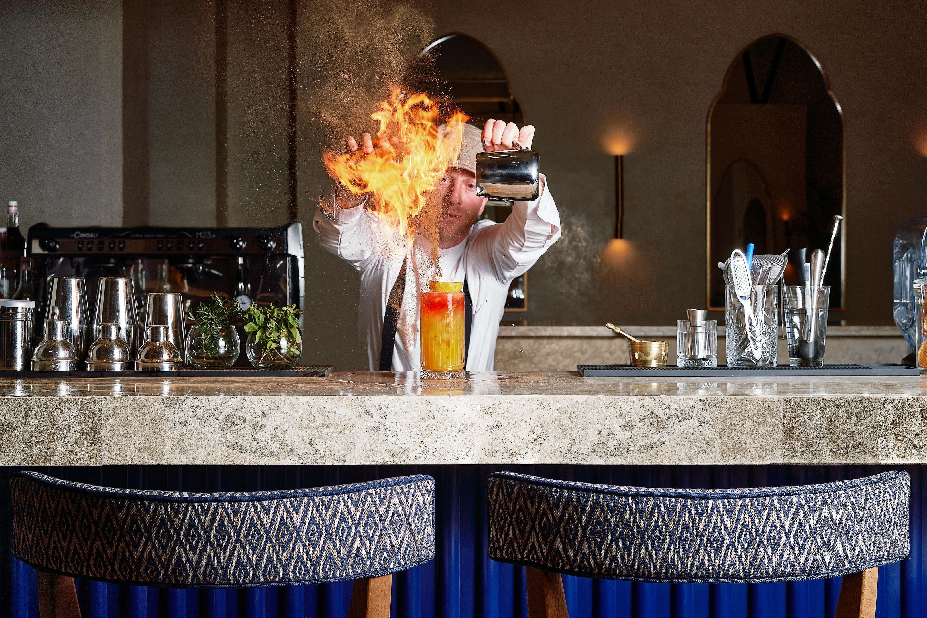 Eine Bar mit einem Barkeeper, der ein Getränk einschenkt, Barutensilien und einer Theke mit Marmorplatte.