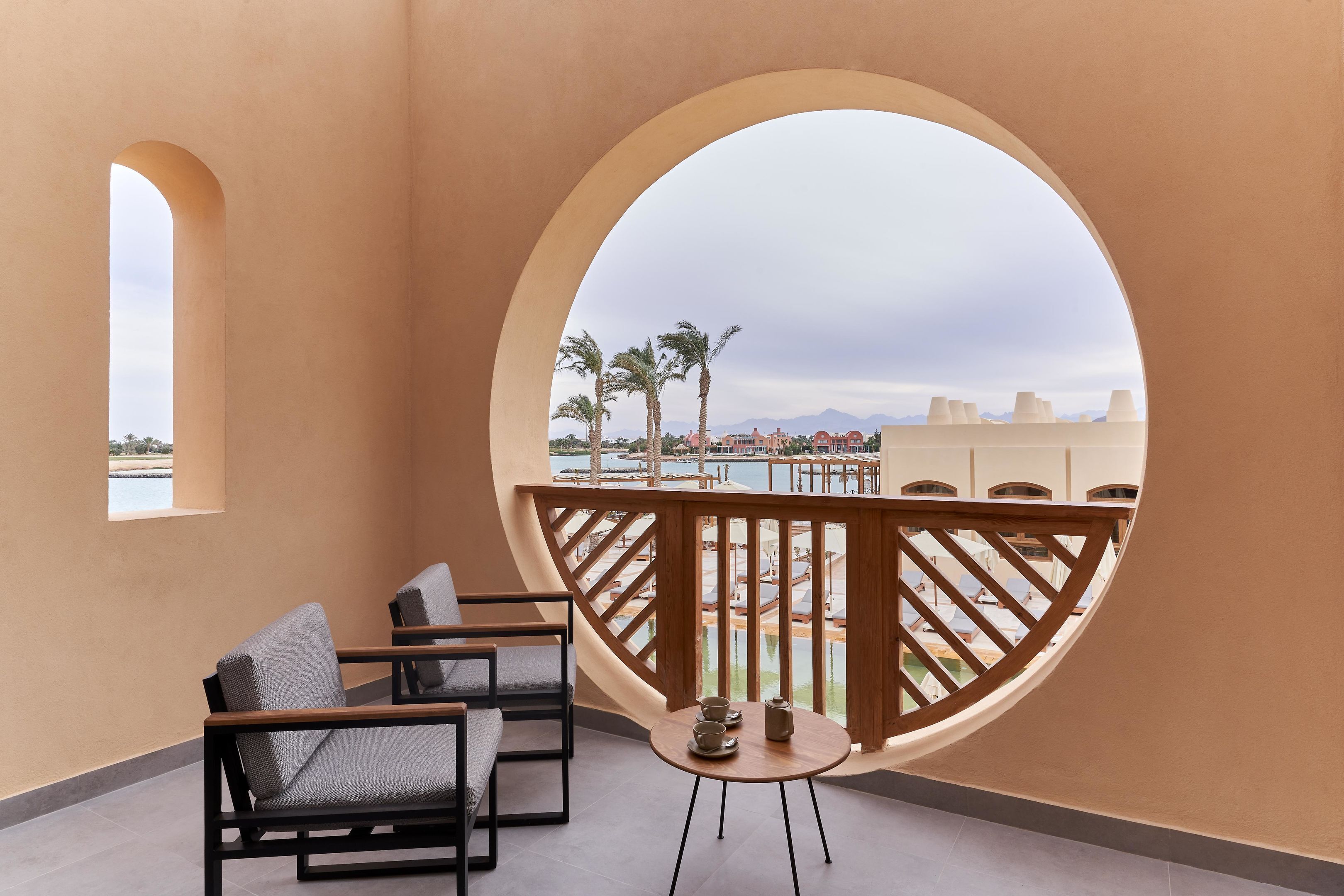 Un balcon avec vue sur une piscine et des palmiers, comprenant deux chaises et une petite table.
