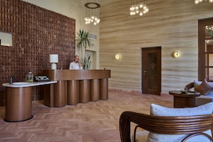 Un área de recepción con un mostrador de madera, una estación de café y un espacio de estar con una silla y una mesita.