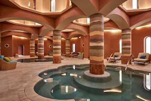 A spa area with a central pool, lounge chairs, and a modern architectural design with curved ceilings and striped columns.