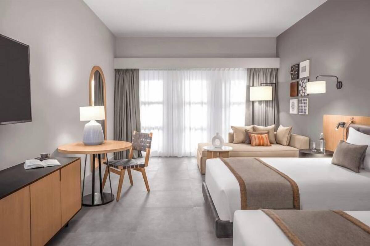 A hotel room with a bed, a sofa, a desk with a lamp, a chair, and a TV.