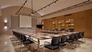 Un salón de conferencias con una larga mesa, sillas, una pantalla de proyector y un atril.