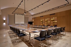 A conference room with a long table, chairs, a projector screen, and a podium.