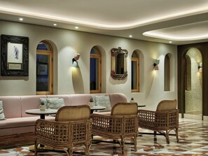 Una habitación con sofá, dos sillas de mimbre, una mesita y un espejo decorativo.