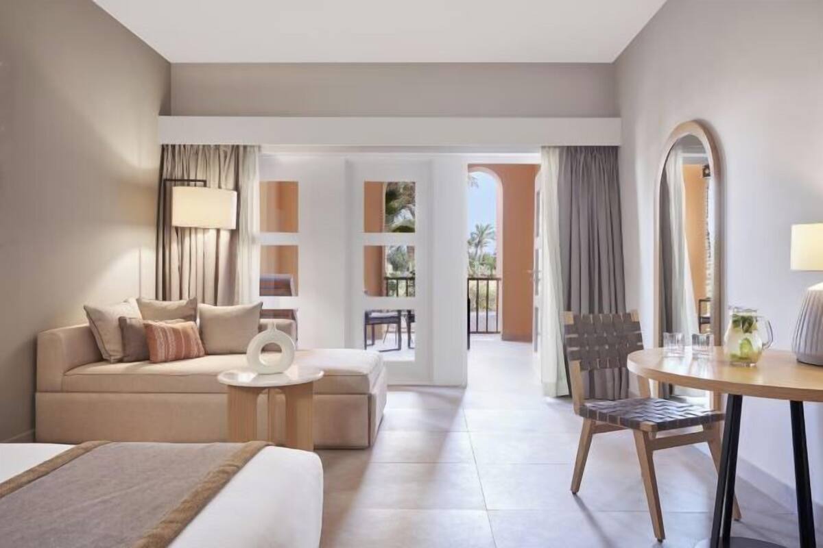 A hotel room with a bed, a sofa, a small table, a chair, and a balcony view.