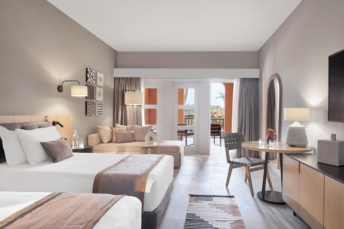 Habitación de hotel con dos camas, un sofá, una mesa de comedor y una televisión.