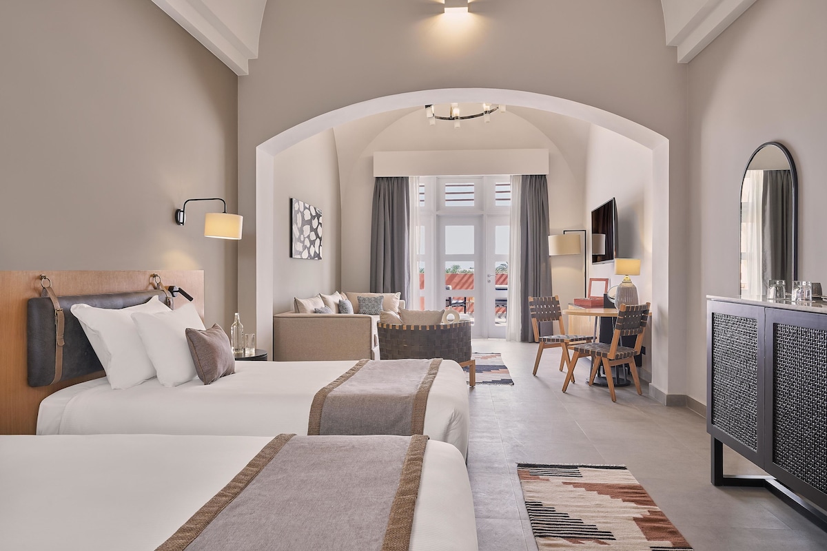Habitación de hotel con dos camas, un escritorio, una silla, un televisor y un espejo grande.