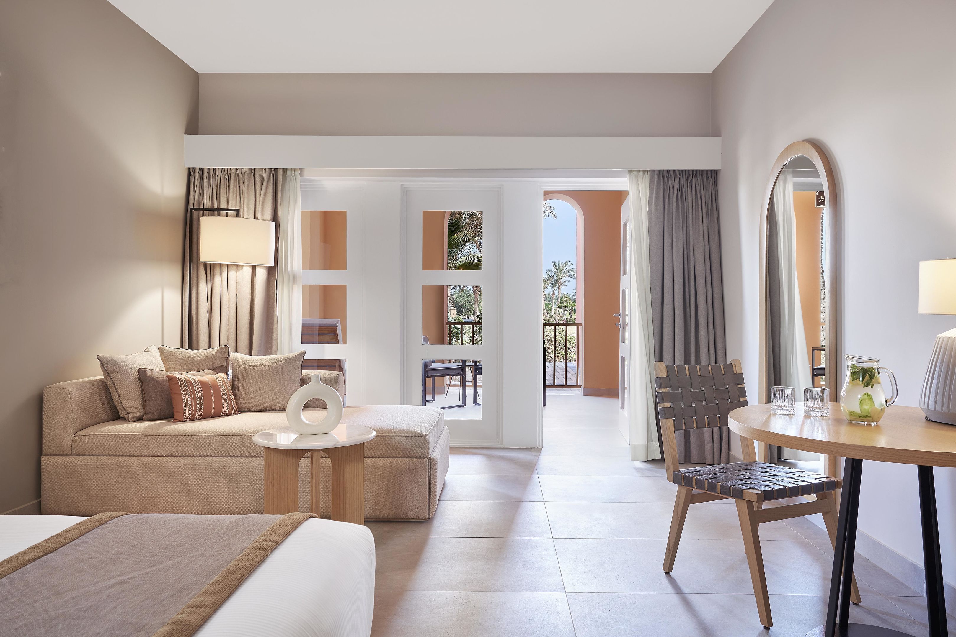 A hotel room with a bed, a sofa, a small table with a lamp, a chair, and a view of the outside.