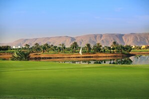 A golf course with a flagstick, palm trees, and a body of water. - Steigenberger Golf Resort El Gouna (El Gouna)