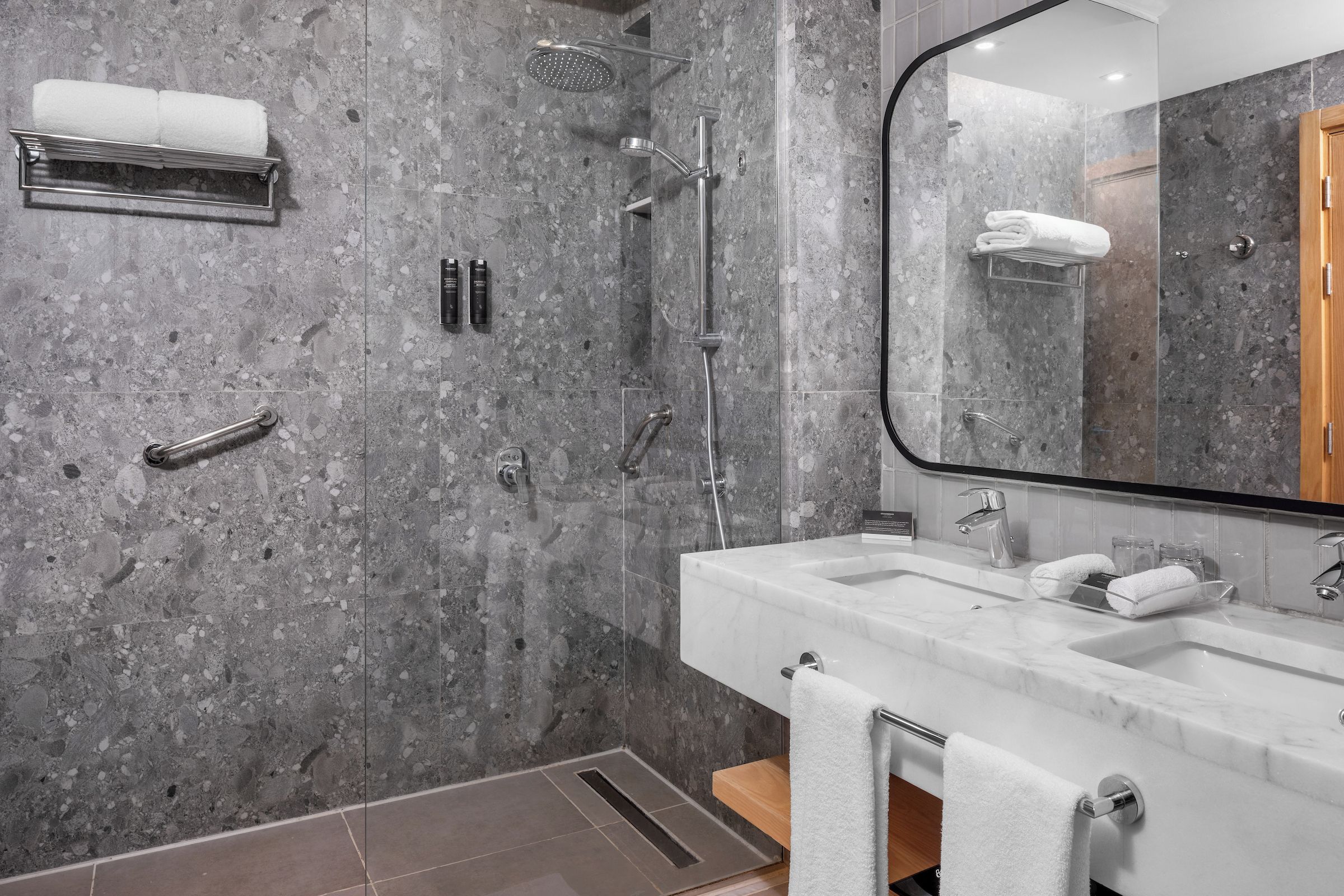 Une salle de bain moderne avec un mur en marbre, un grand miroir, un lavabo et un espace douche.