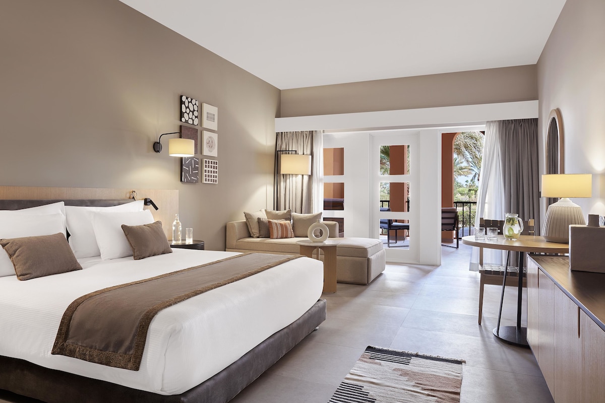 Una habitación de hotel moderna con una cama grande, un sofá, un comedor y vistas al exterior.