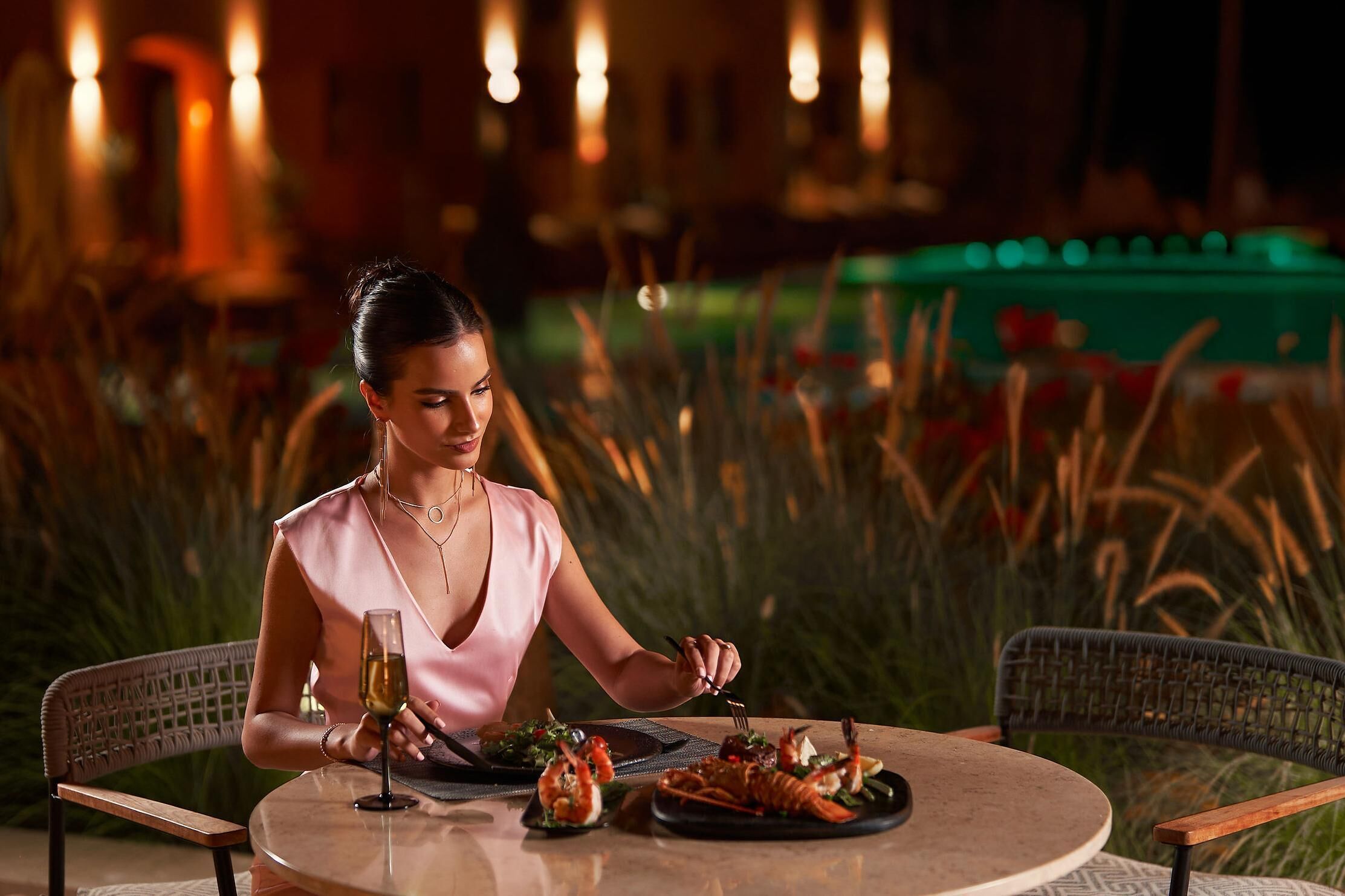 A woman dining at an outdoor table with a glass of wine, surrounded by chairs and a table setting with seafood dishes.