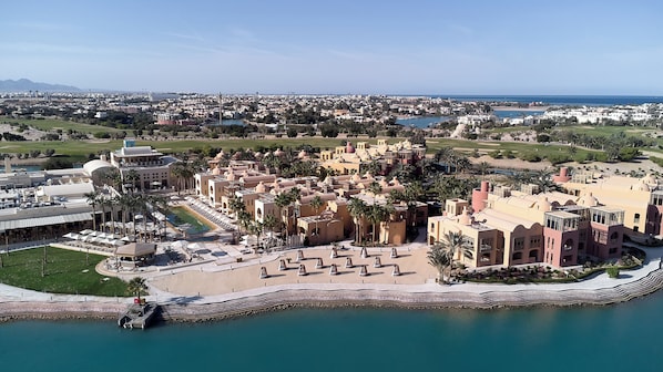 Luchtbeeld van een resort met een zwembad, palmbomen en een strand.