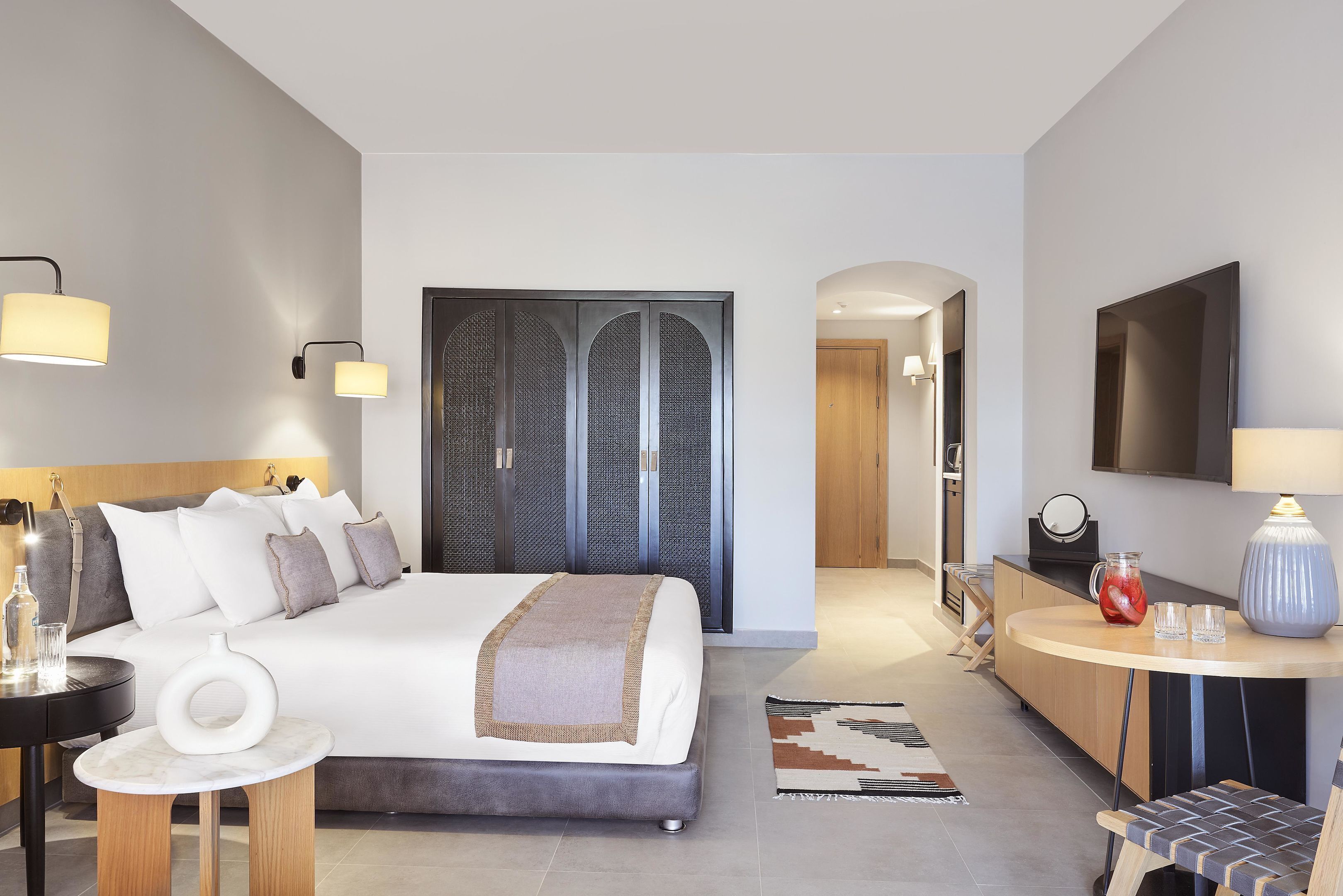 A modern hotel room with a large bed, bedside tables, a desk, and a TV.