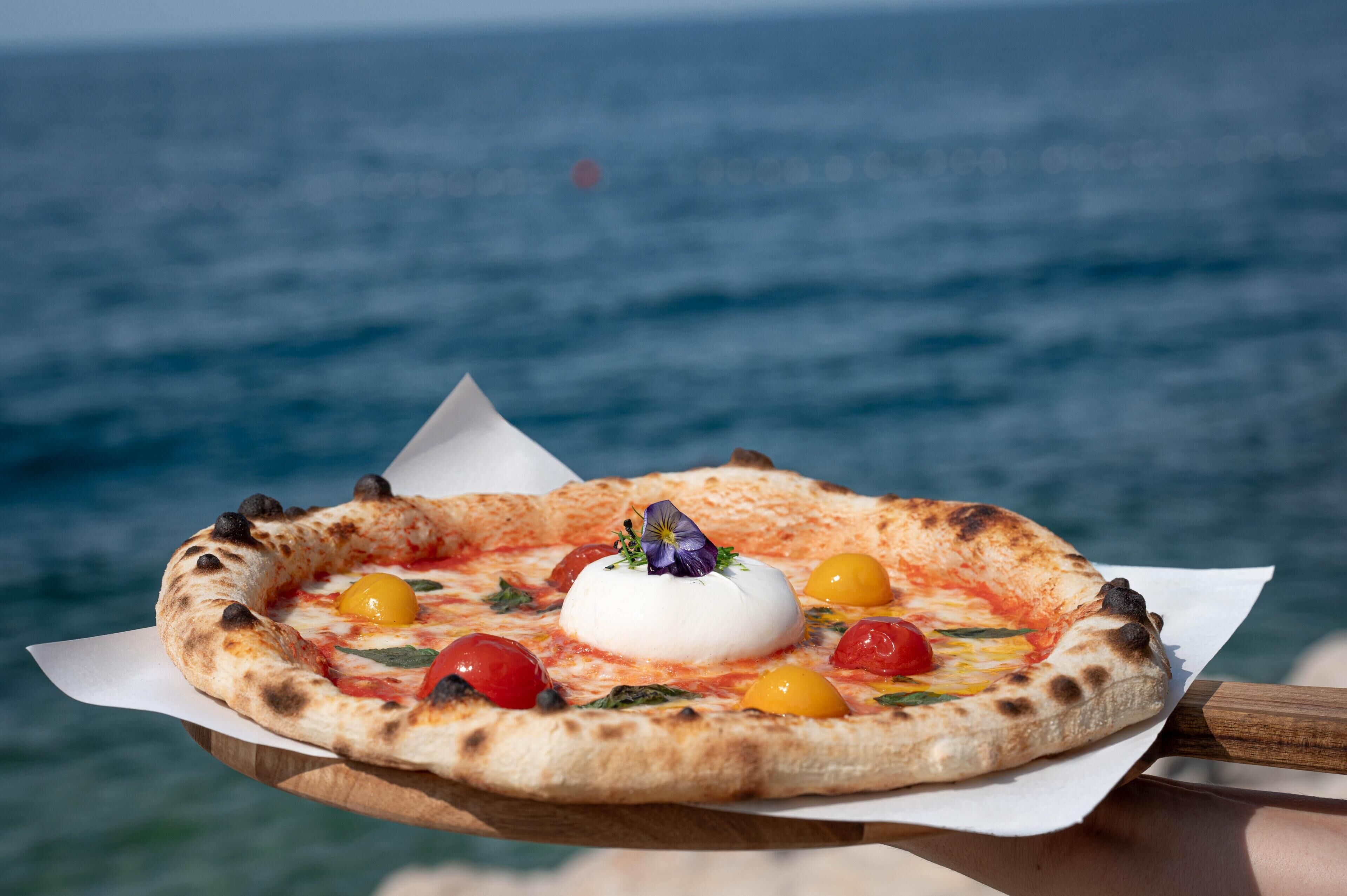 A pizza with toppings and a flower on a wooden board.