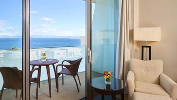A balcony with a view of the sea, a table with chairs, a vase with flowers, and a lamp.
