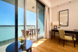 A hotel room with a balcony, a desk, a chair, and a table with flowers.