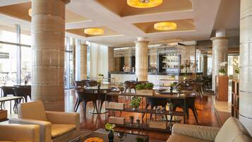 A spacious lobby with high ceilings, large pillars, and a central bar area. There are seating arrangements and a variety of plants.