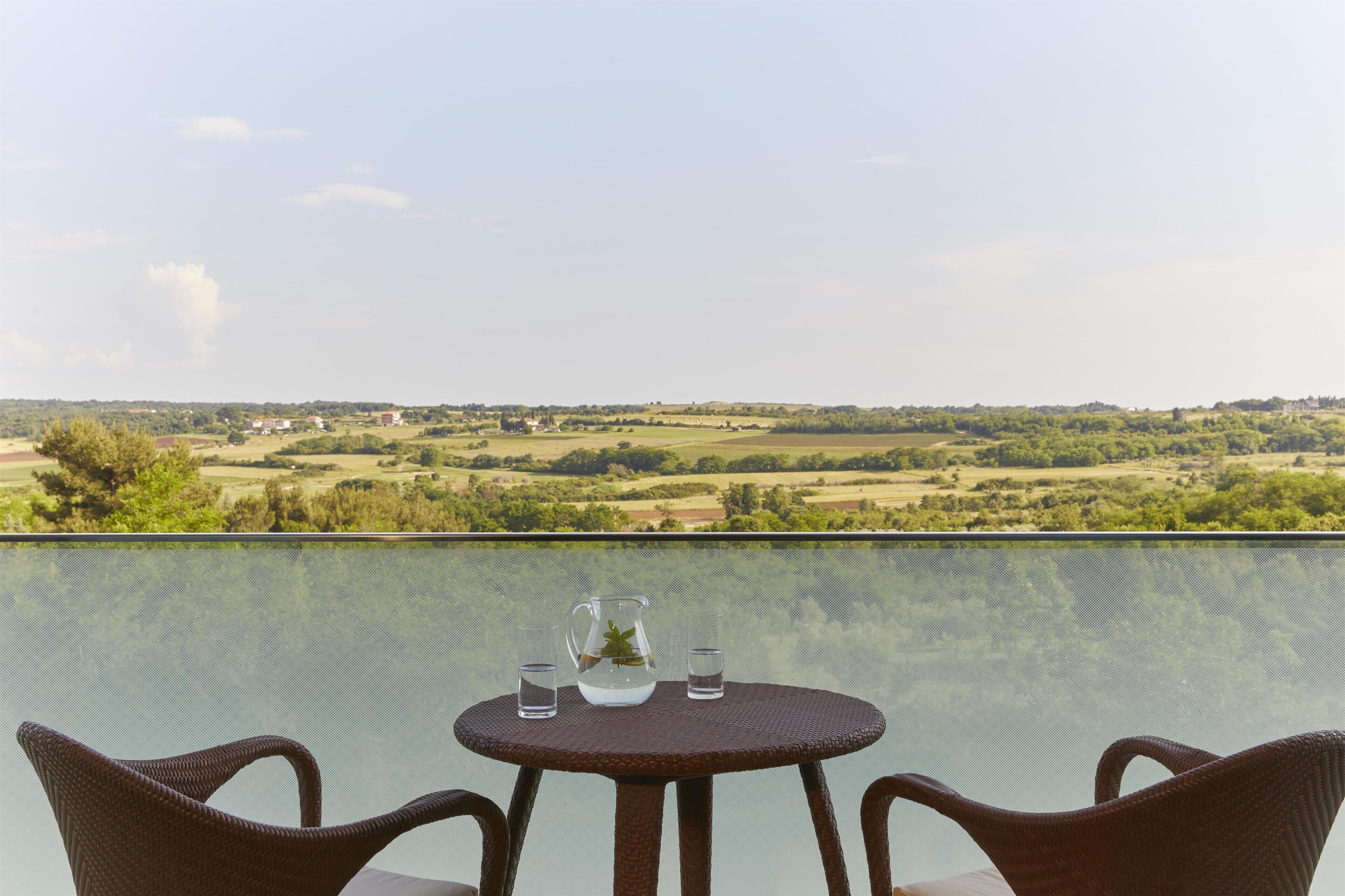 Een tafel met twee stoelen en een waterkan op een balkon met uitzicht op een prachtig landschap.