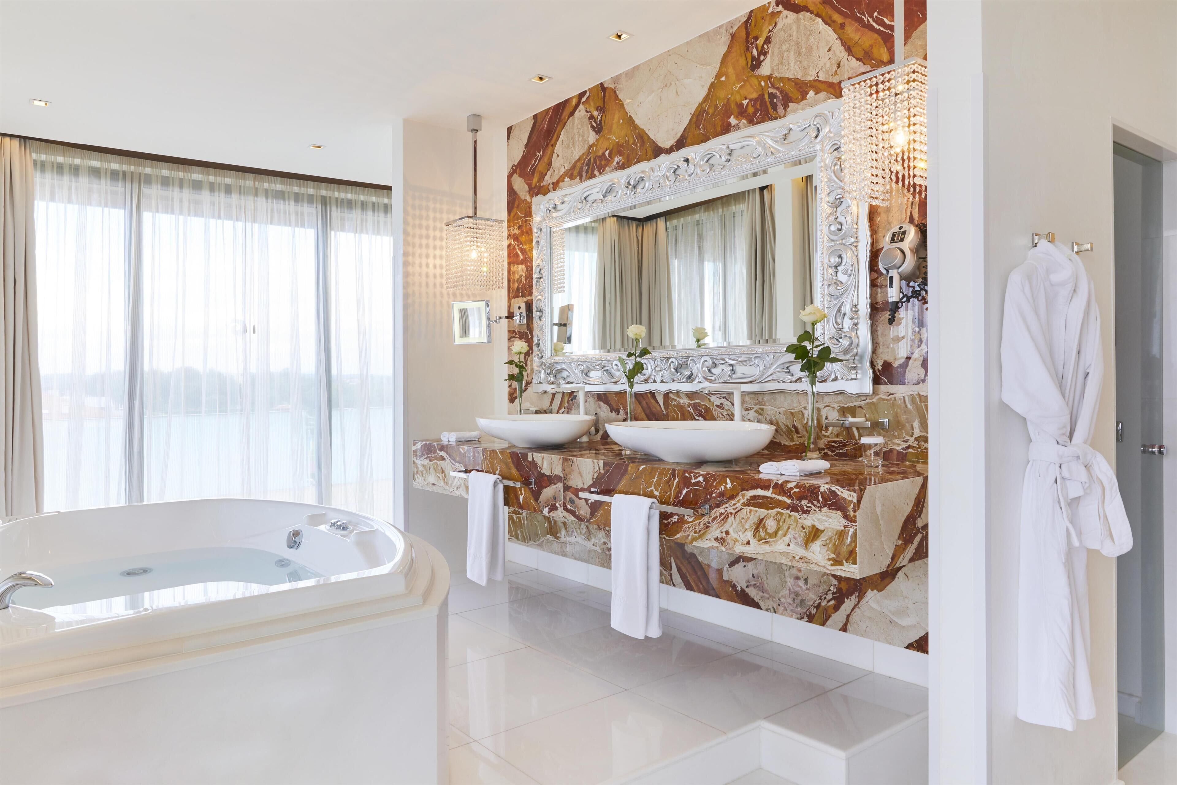 A modern bathroom with a large bathtub, two sinks, and a marble backsplash.