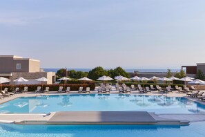 En swimmingpool med solstolar och parasoller, omgiven av byggnader och med utsikt över havet.
