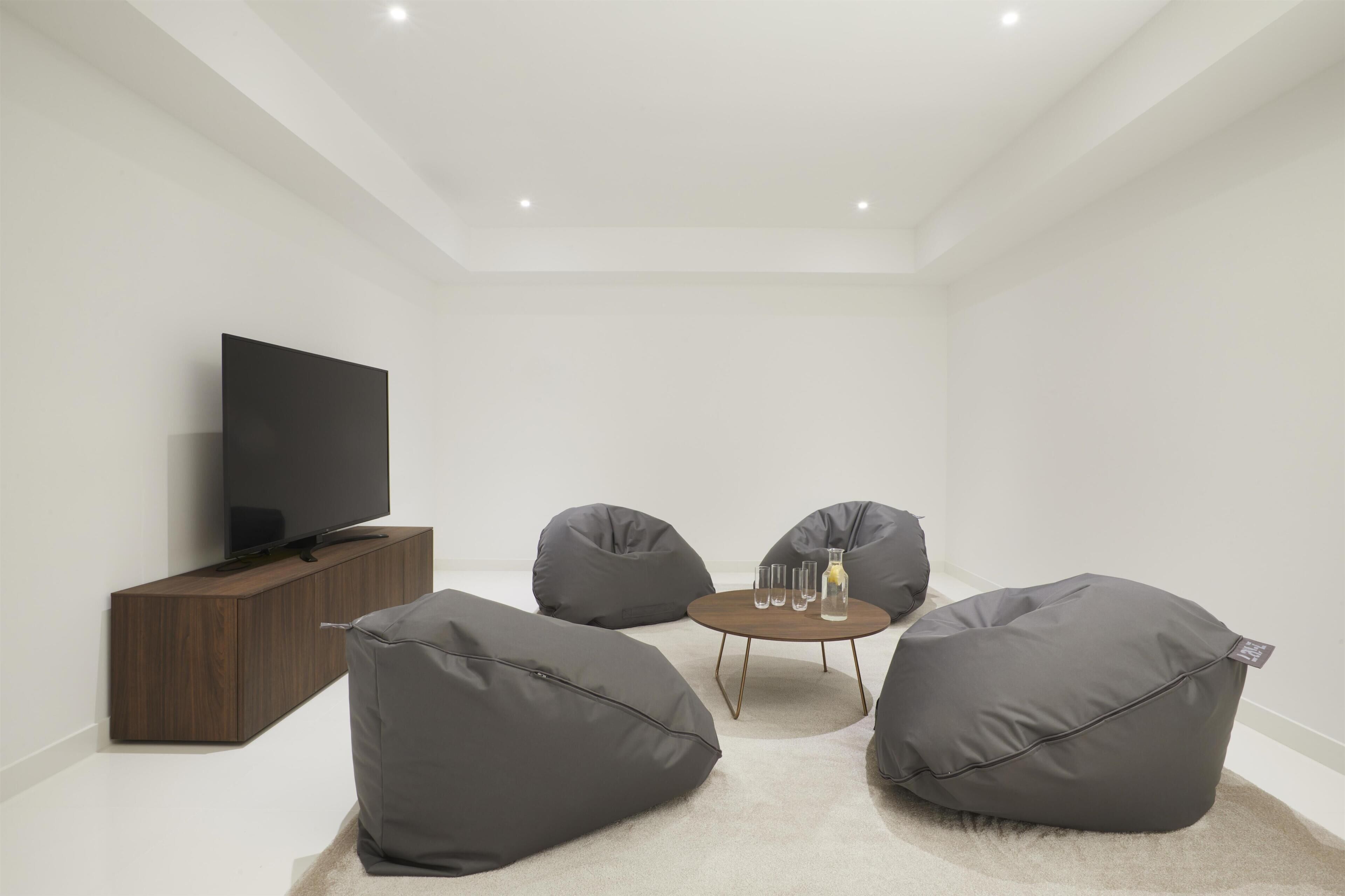 Un salon moderne avec un téléviseur à écran plat, des fauteuils en forme de poire de couleur gris foncé, une petite table ronde avec des boissons et un meuble en bois.