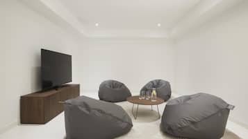Un salon moderne avec un téléviseur à écran plat, des fauteuils en forme de poire de couleur gris foncé, une petite table ronde avec des boissons et un meuble en bois.