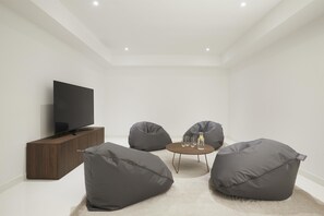 A modern living room with a flat-screen TV, dark grey bean bag chairs, a small round table with drinks, and a wooden cabinet. - Adriatic Istria Resort Operated by Minor Hotels (Umag)
