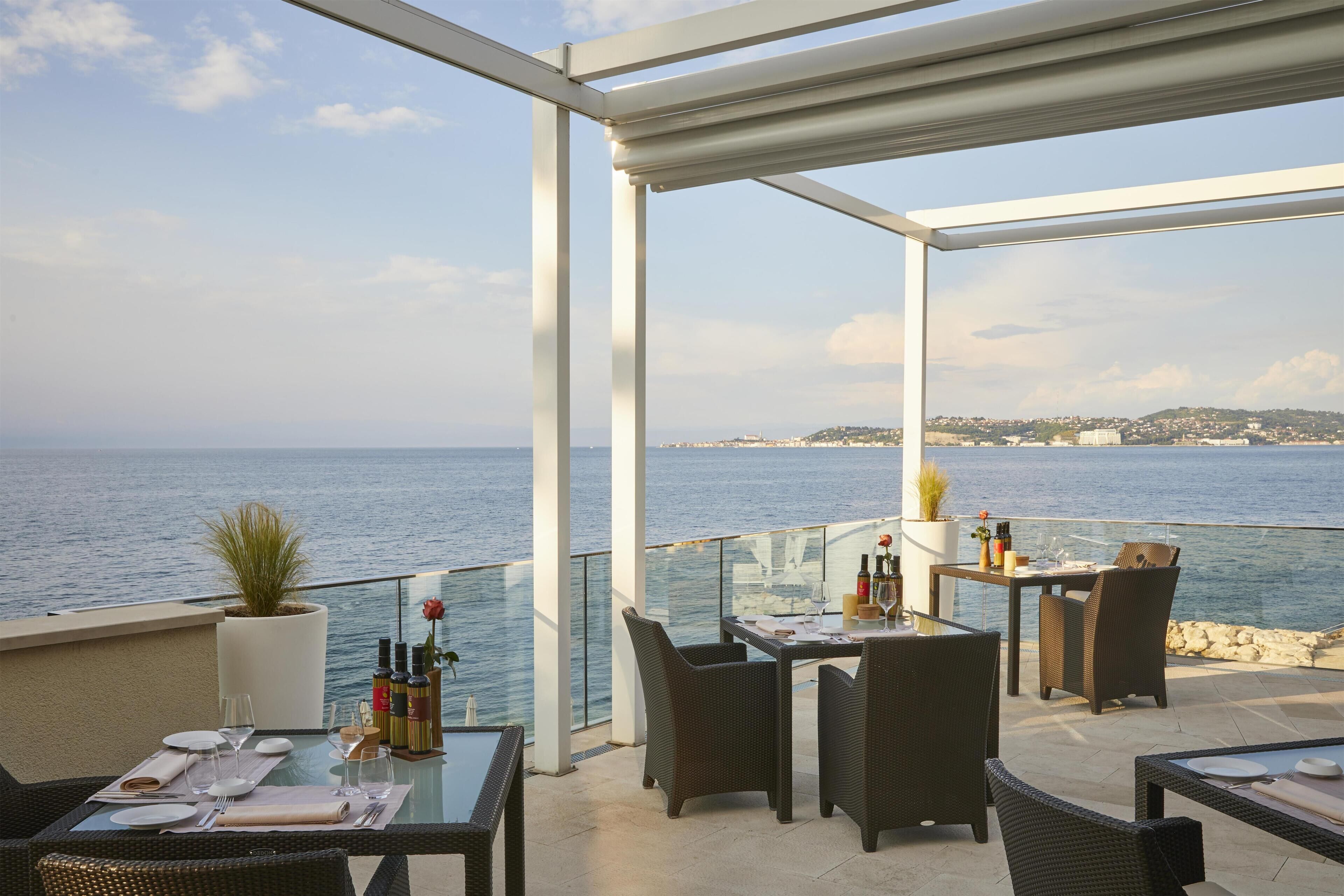 An outdoor dining area with tables and chairs, overlooking the sea.