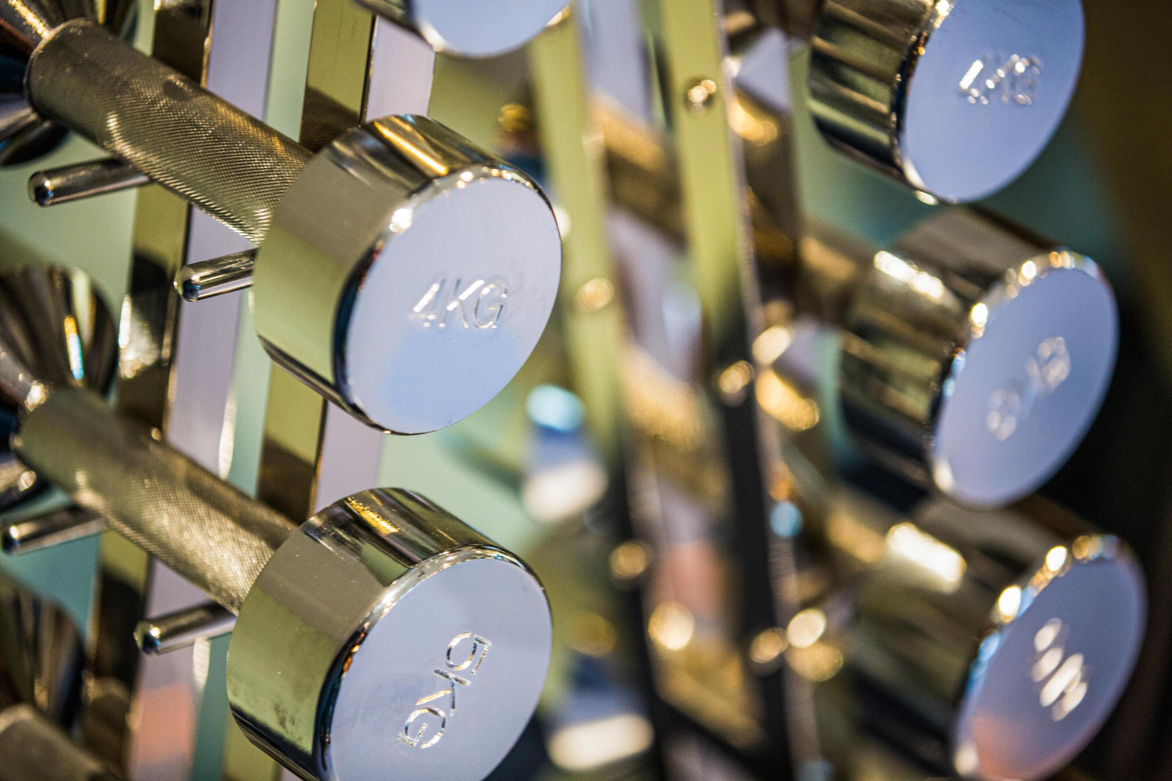 A close-up of a series of metallic dumbbells with weight markings, indicating a gym setting.