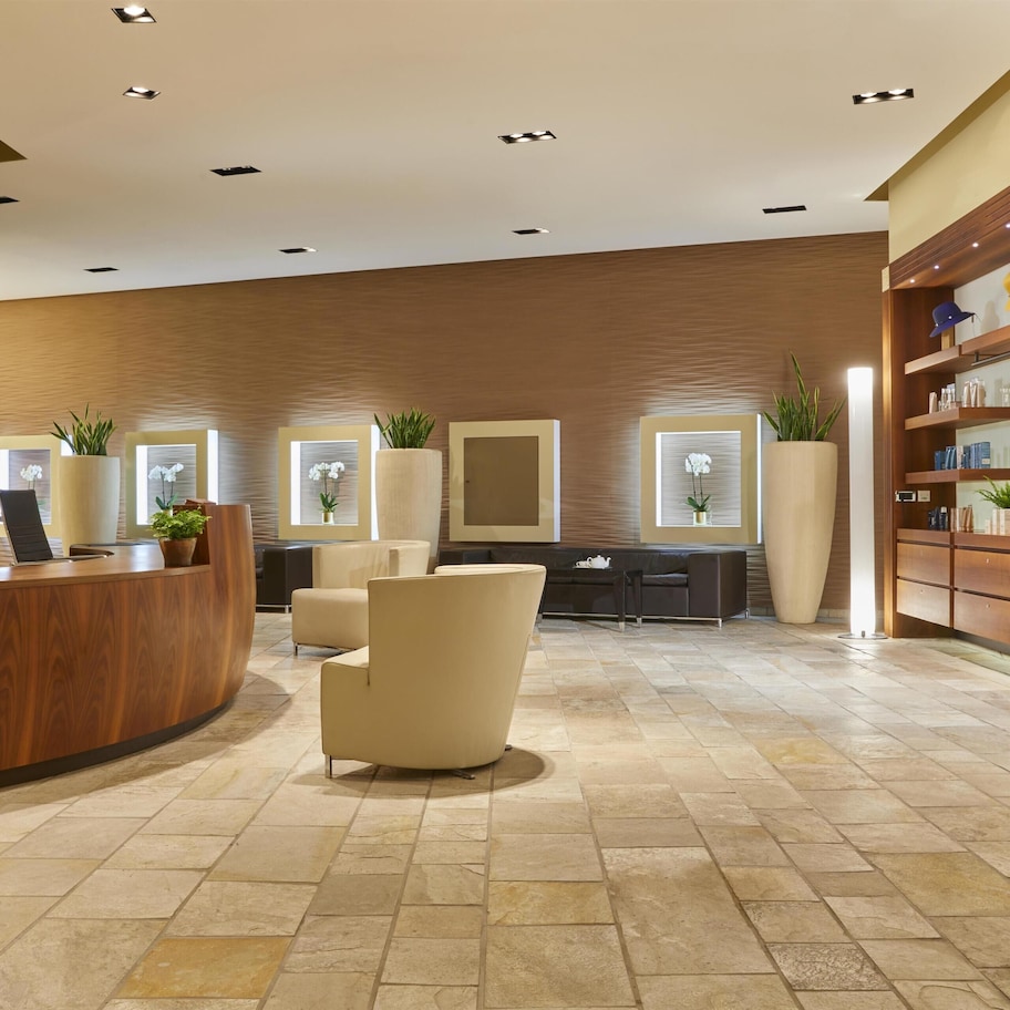 A reception area with a wooden reception desk, beige armchairs, and a large potted plant.