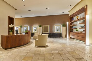 Una zona de recepción con un mostrador de madera, sillones color beige y una planta grande en maceta.